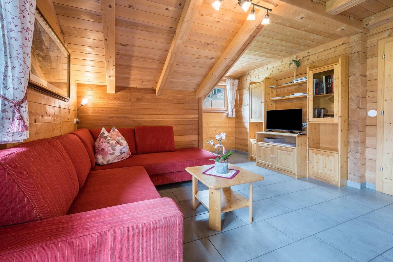 Wohnzimmer der Ferienwohnung mit rotem Sofa, Holzwänden und Fernseher